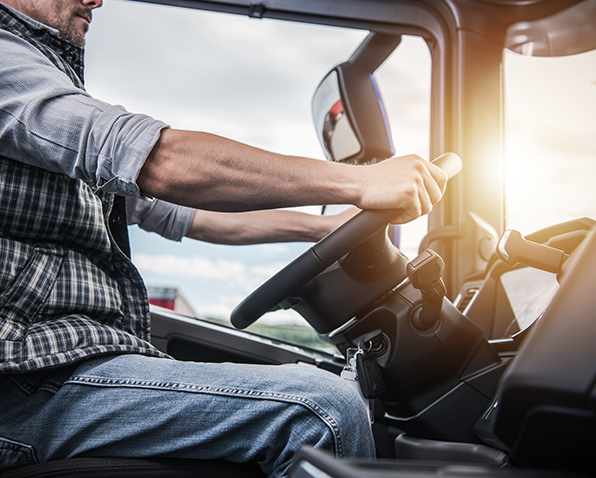 A closeup of a truck driver seated in their truck holding onto the steering wheel.