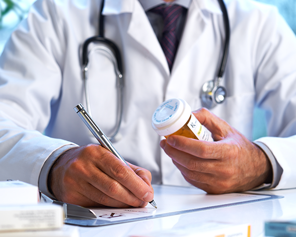 A doctor writing a prescription while holding a bottle of pills.
