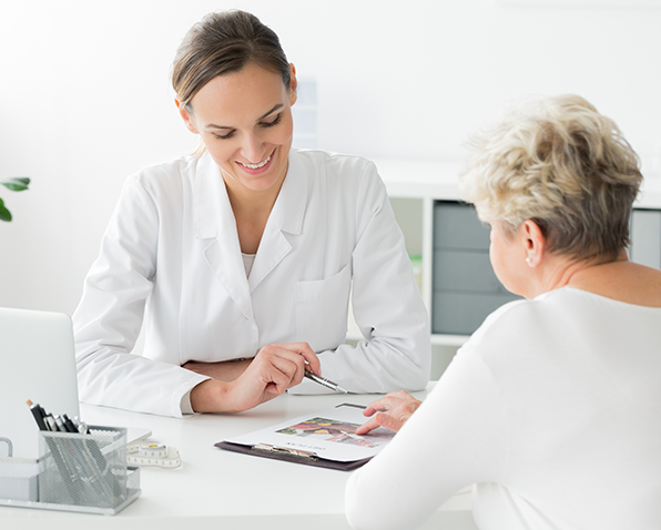 A doctor looking at a clipboard with a patient at her desk.