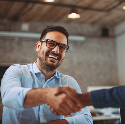 A man in glasses smiling while shaking another person's hand who is out of the frame.